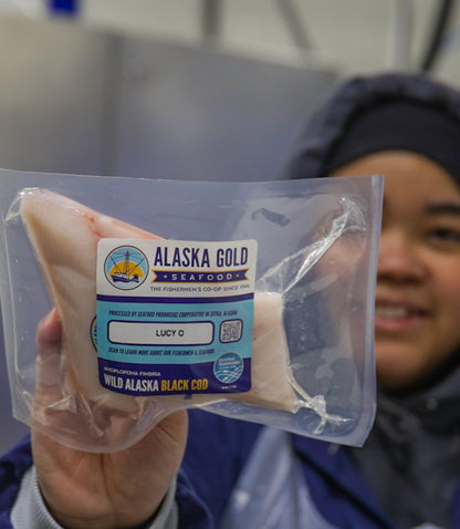 Worker holding black cod fillet with boat name on label