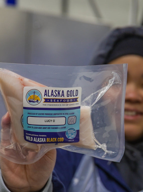 Worker holding black cod fillet with boat name on label