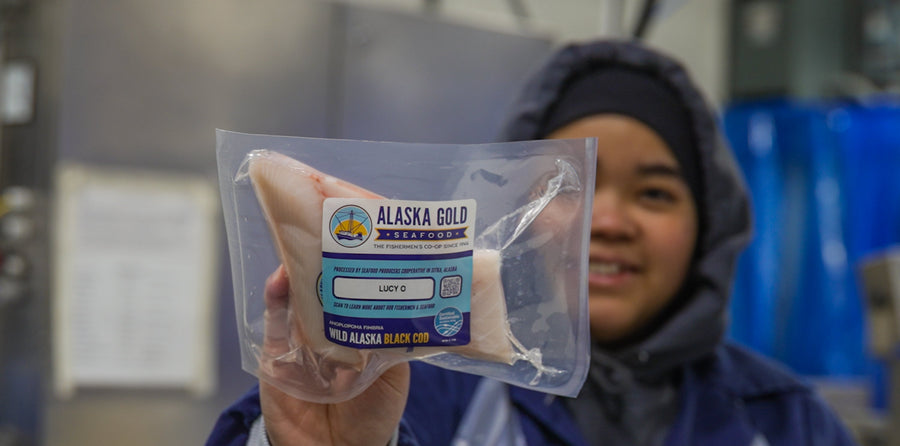Worker holding black cod fillet with boat name on label