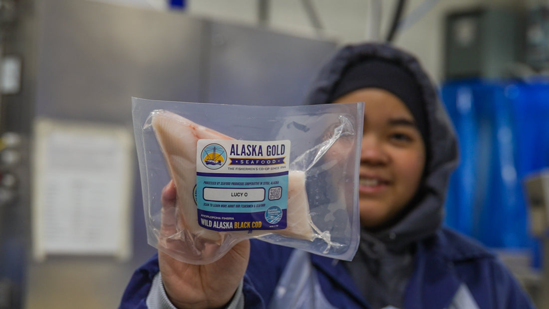 Worker holding black cod fillet with boat name on label
