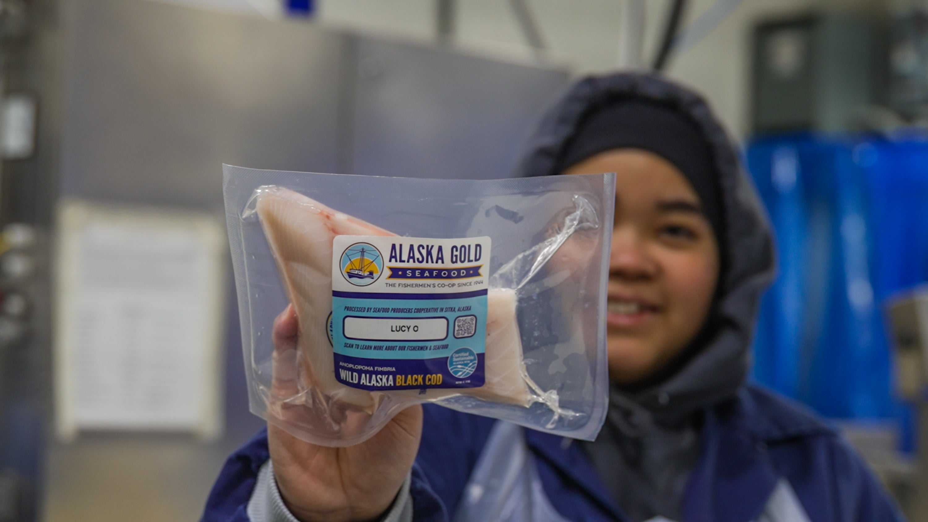 Worker holding black cod fillet with boat name on label